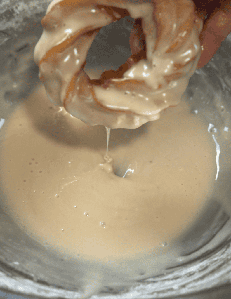 Hand dipping a homemade donut into a creamy batter for baking.