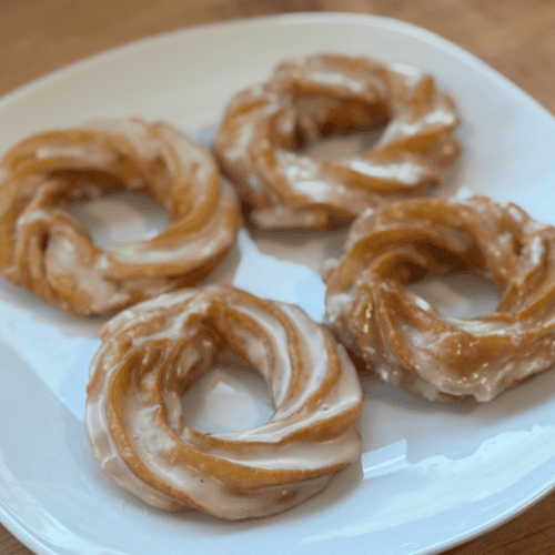 Fresh glazed donuts on a white plate, ready to enjoy.