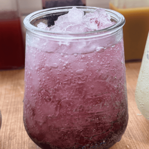 Bright pink berry lemonade served over ice in a clear glass.