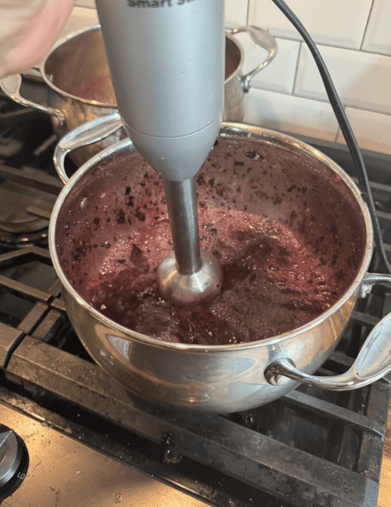 Handheld immersion blender blending fresh berries in a pot for homemade jam.