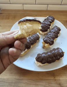Eclairs topped with rich chocolate glaze on a white plate, showcasing fresh homemade pastries.