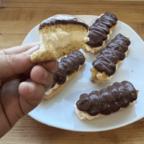 Eclairs topped with rich chocolate glaze on a white plate, showcasing fresh homemade pastries.