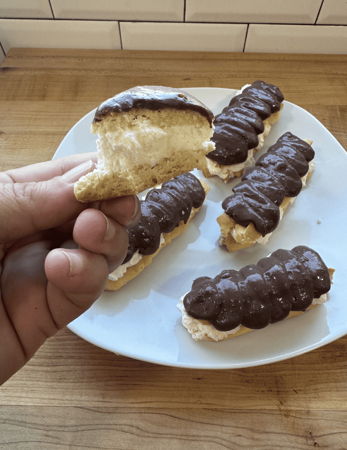 Eclairs topped with rich chocolate glaze on a white plate, showcasing fresh homemade pastries.