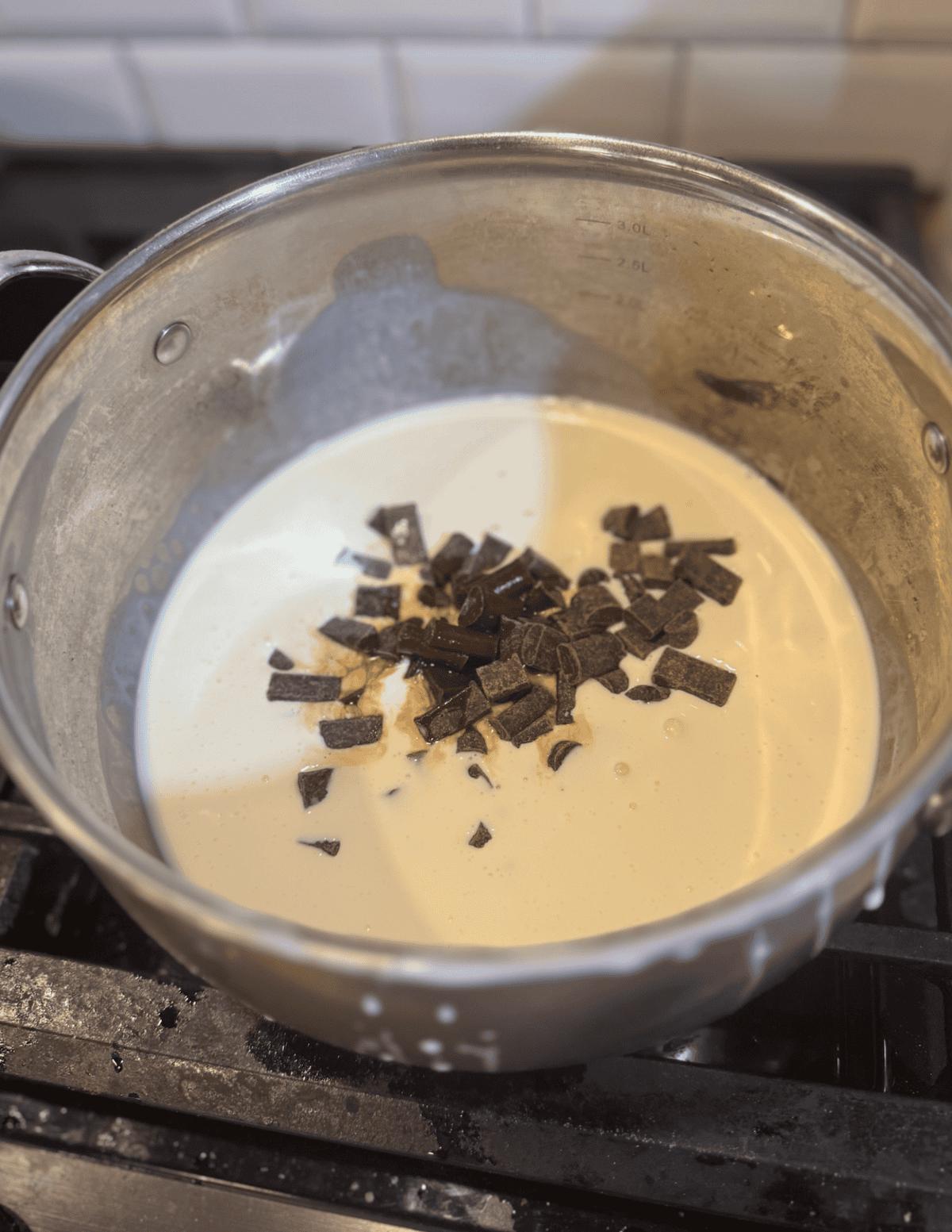 Creamy chocolate sauce with chopped dark chocolate pieces in a saucepan, ready for dessert or baking.
