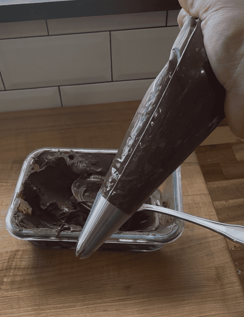 Homemade chocolate ice cream being piped into a container with a piping bag.