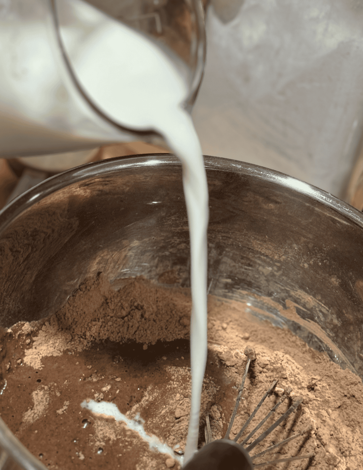 Fresh milk being poured into a mixing bowl with chocolate batter for baking.