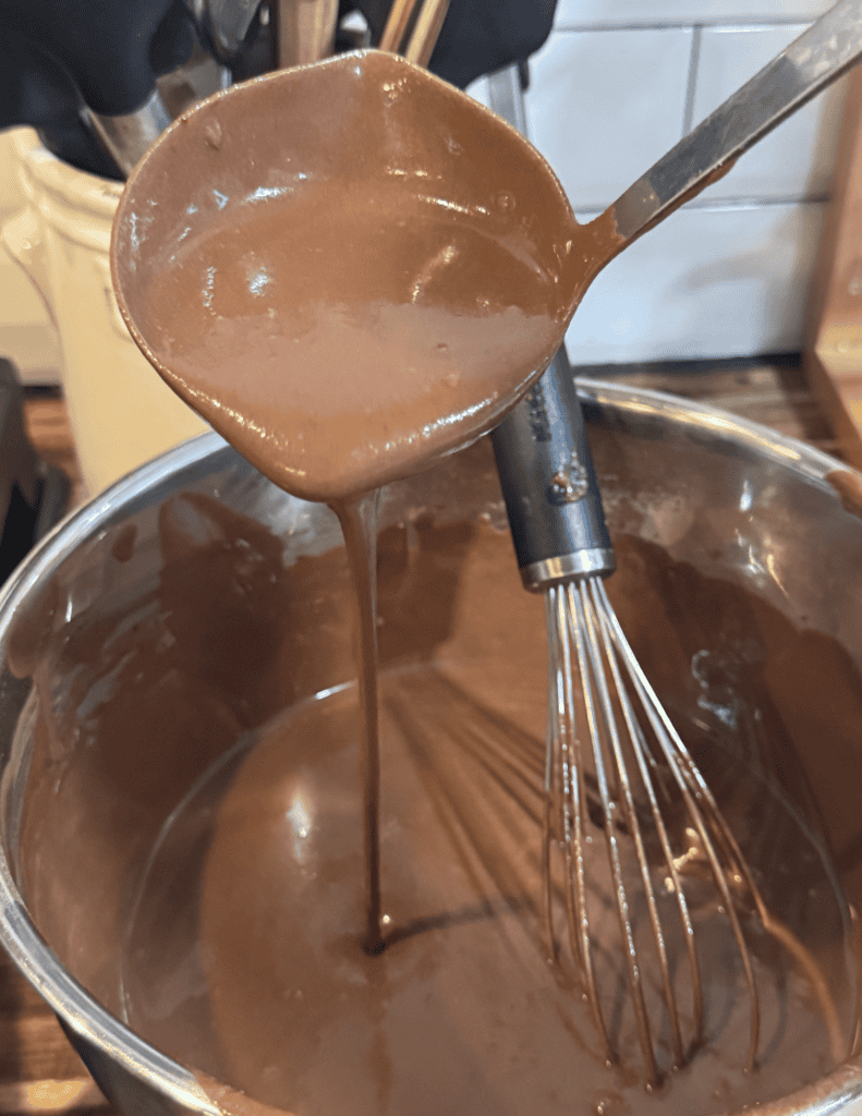 Creamy homemade chocolate fudge being poured from a spoon into a mixing bowl.