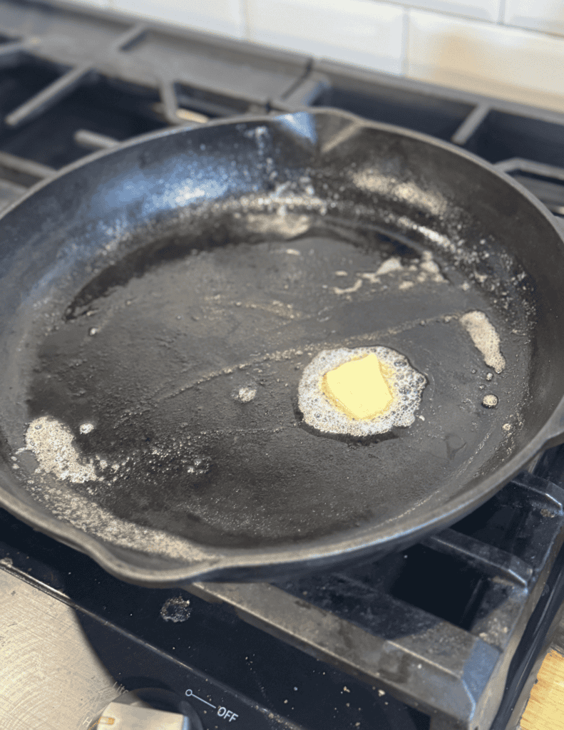 Butter melting in a black skillet on a stovetop.