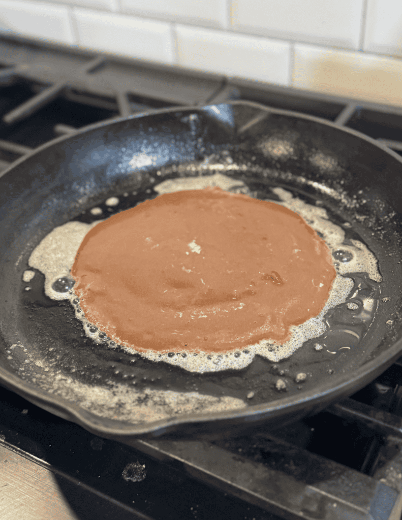 Delicious pancake batter cooking in a non-stick skillet on a stovetop.
