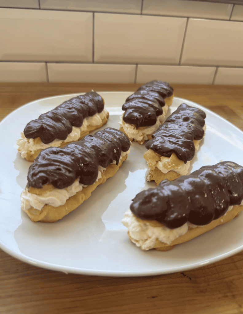 Eclairs topped with rich chocolate and filled with creamy vanilla custard, showcasing fresh, homemad.