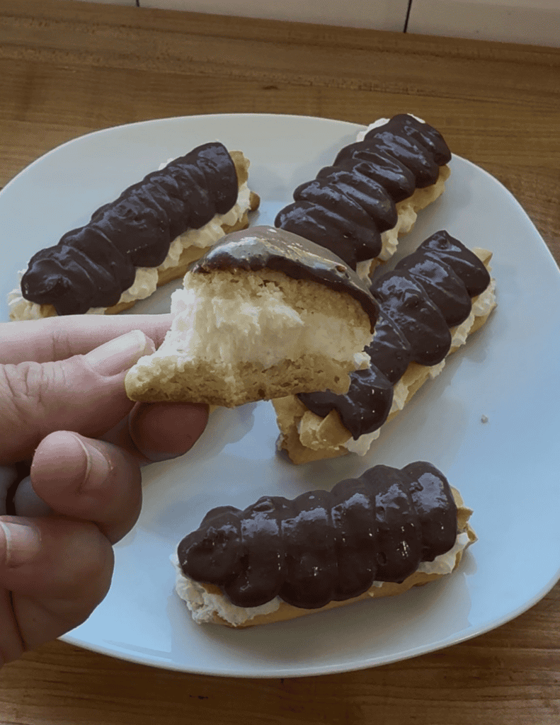 Delicious homemade eclairs topped with rich chocolate glaze on a white plate. Perfect for dessert or.