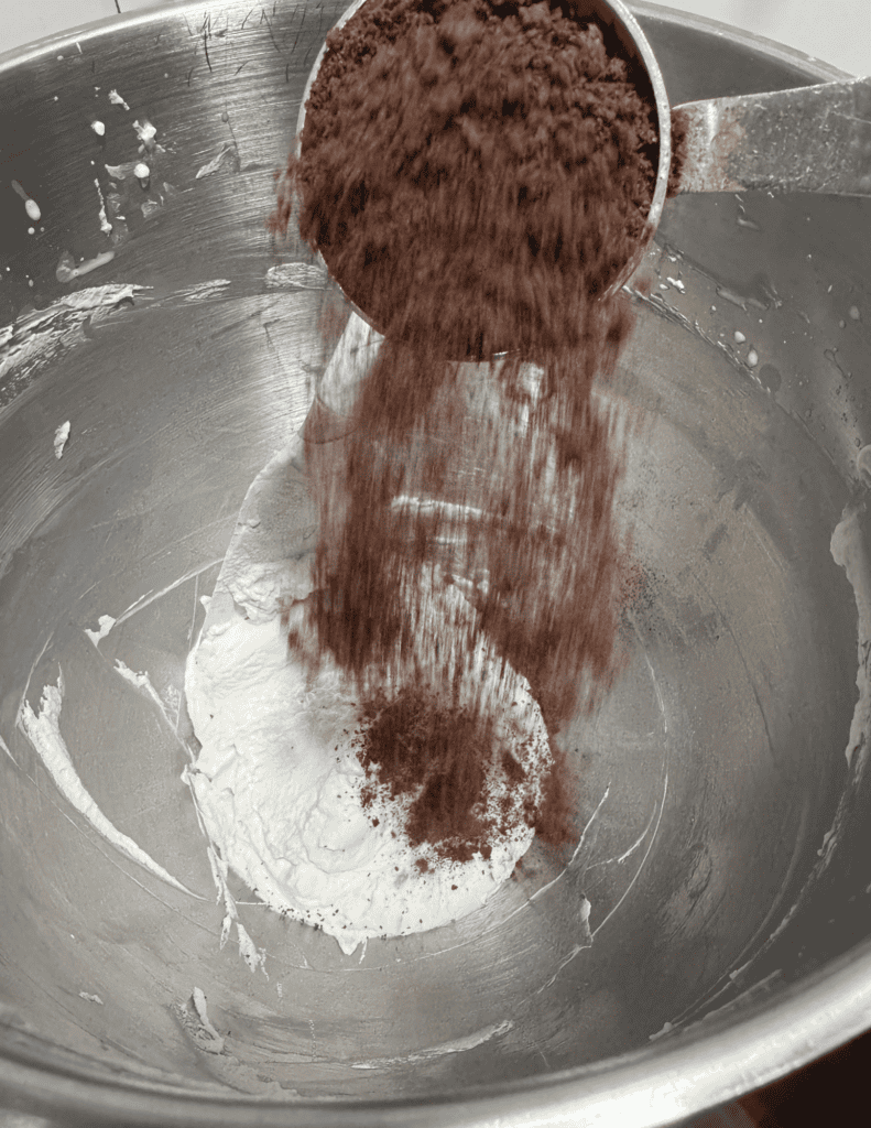 Pouring cocoa powder into mixing bowl with flour and butter for baking.