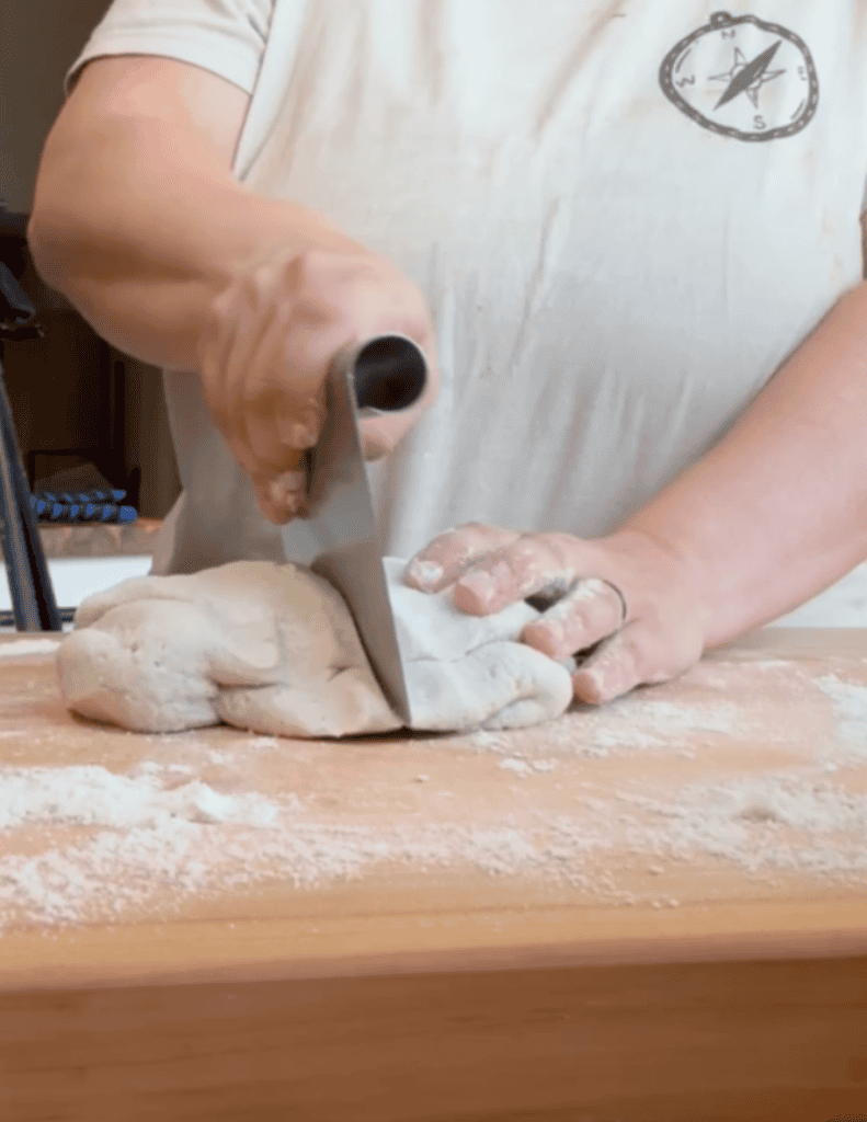 Person cutting homemade dough on a floured wooden surface.
