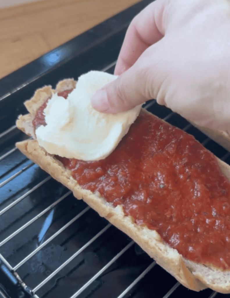 Hand placing dollop of sour cream on homemade tomato pie with crust on baking rack.
