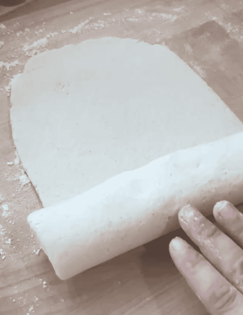 Fresh homemade dough being rolled out on a floured surface.