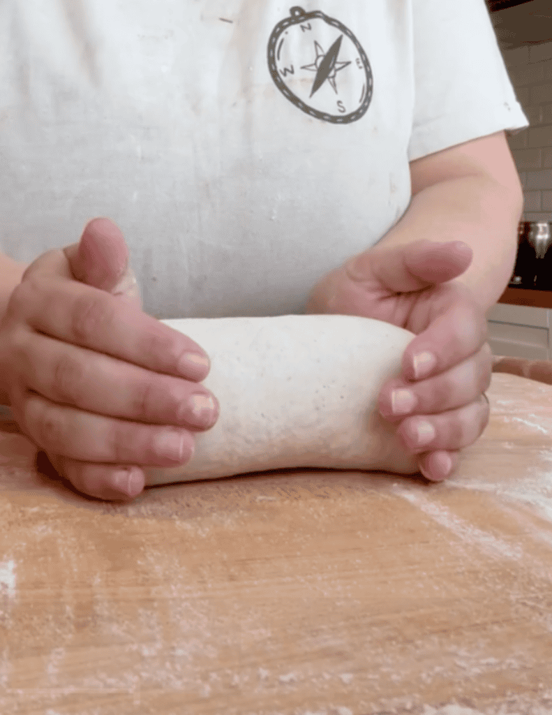 Person shaping dough on a wooden surface, emphasizing fresh homemade baking.