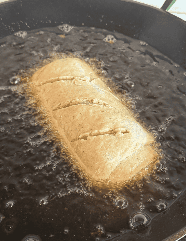 Fresh homemade bread frying in a skillet with bubbling oil.