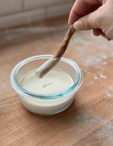 Hand dipping breadstick into creamy homemade dairy dip in glass bowl.