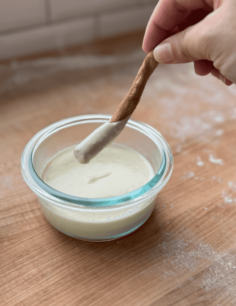 Hand dipping breadstick into creamy homemade dairy dip in glass bowl.