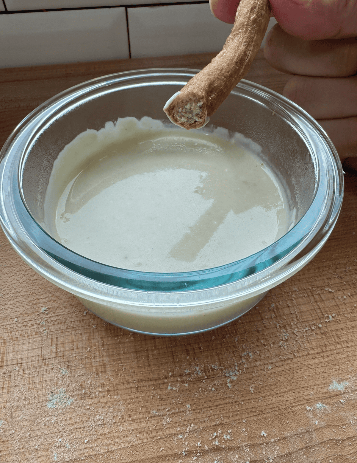 Hand dipping a breadstick into a bowl of creamy dairy-free yogurt.