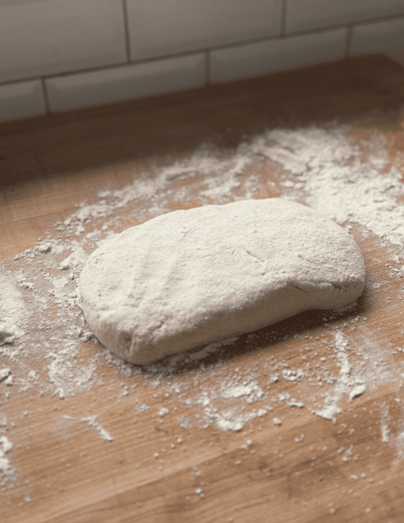 Fresh homemade bread dough on a wooden surface with flour.