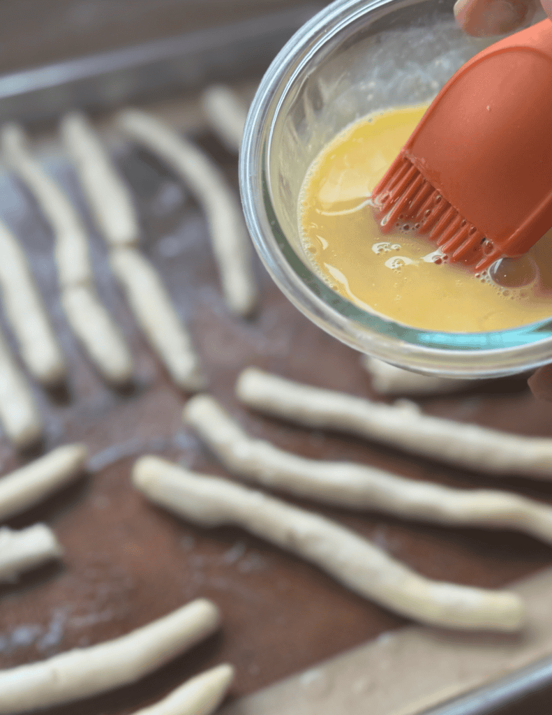 Applying egg wash to pastry dough with a silicone brush for a golden finish.