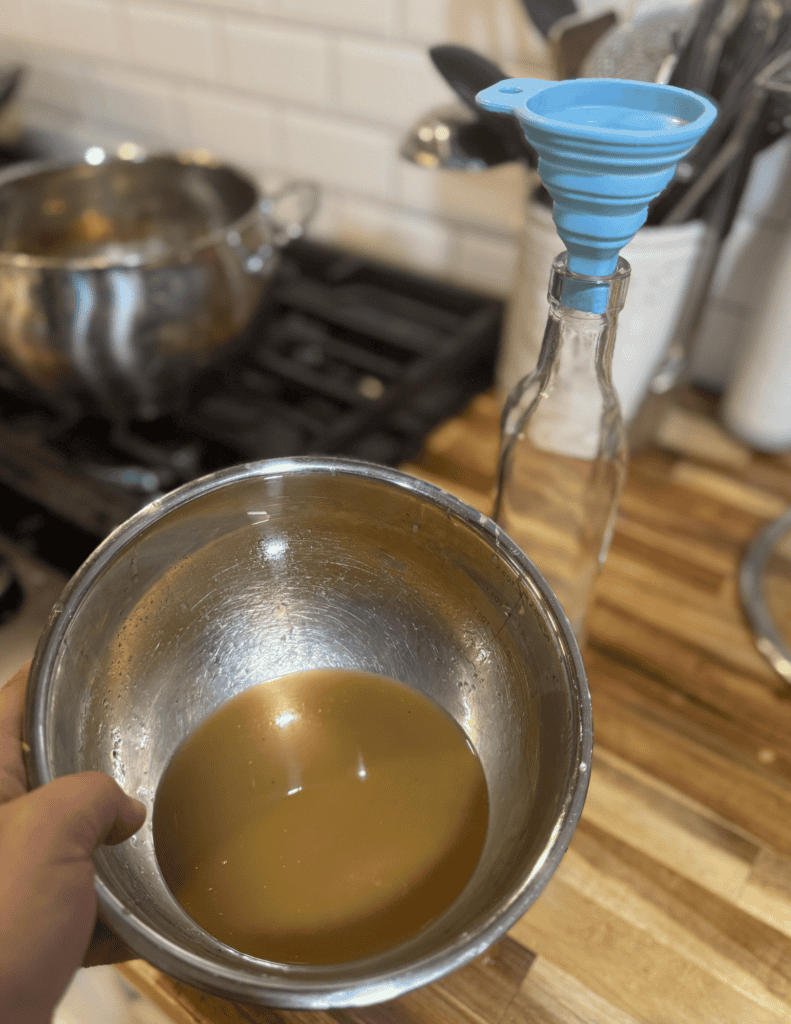 Hand holding a bowl of homemade broth in a kitchen setting.