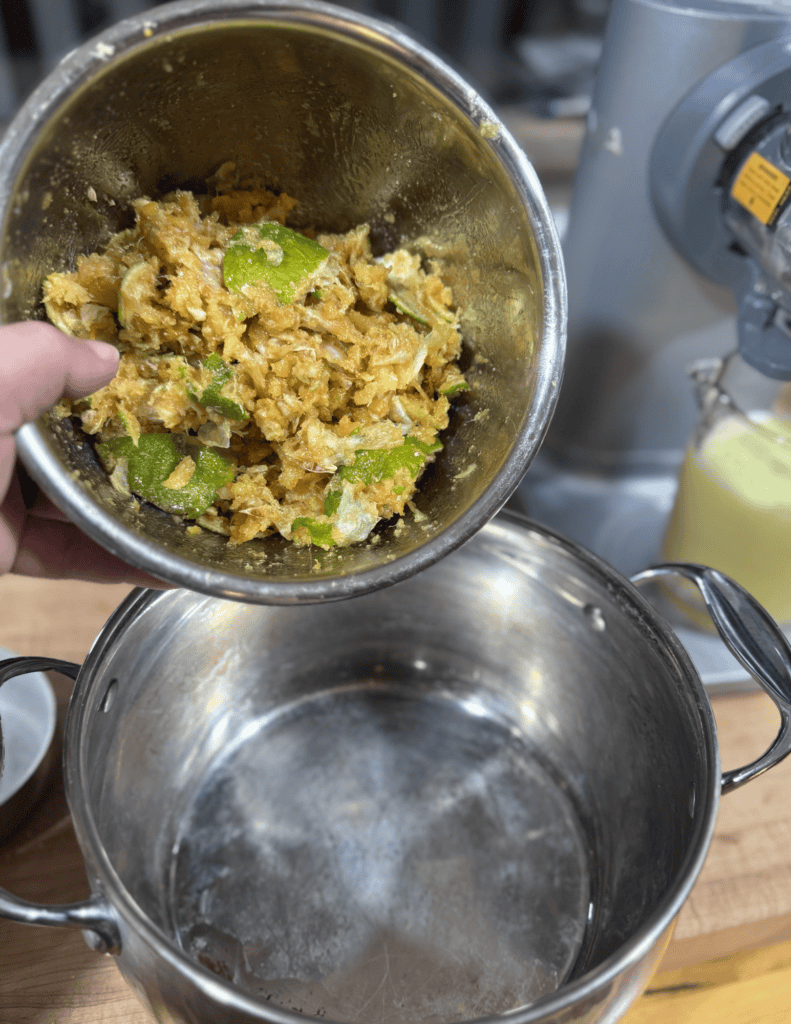 Hand pouring mashed vegetables into a pot in a farm-fresh kitchen setting.