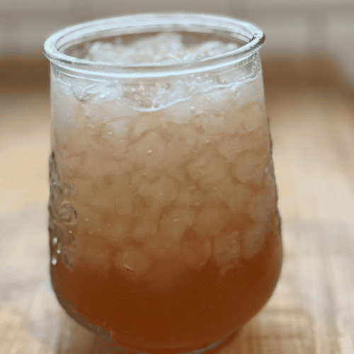 Glass of homemade lemonade with ice, served in a rounded glass on a wooden surface.