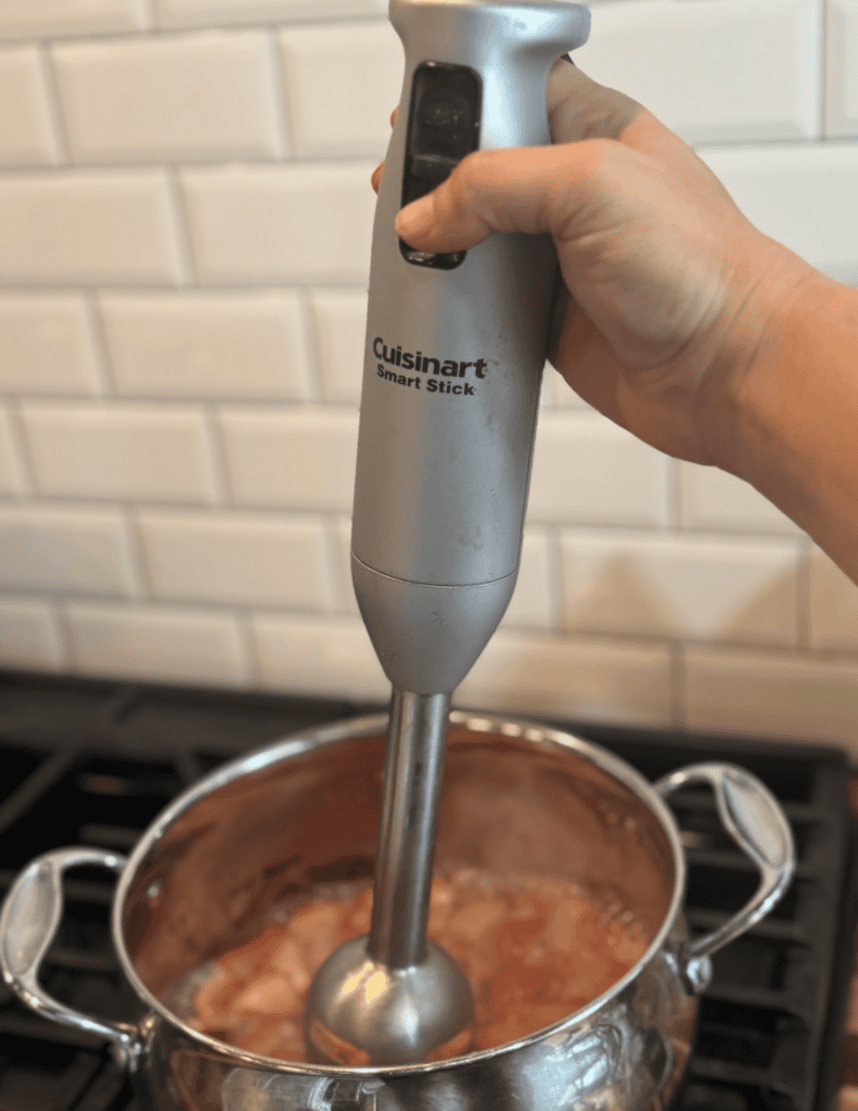 Immersion blender blending cooked ingredients in a pot on stove.