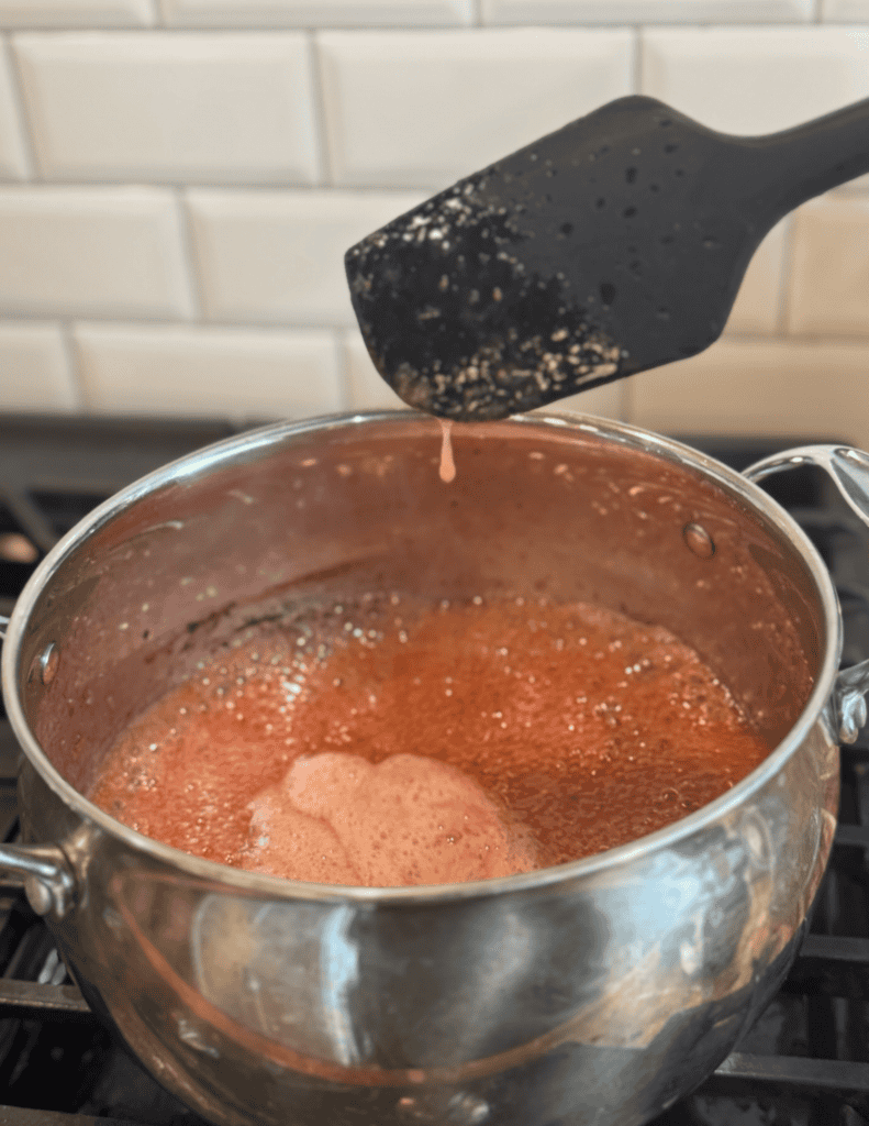 Boiling sauce in a stainless steel pot on a stove with a black spatula.