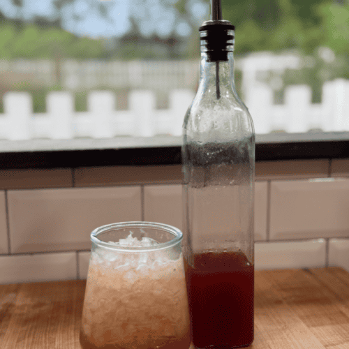 Fresh fruit juice served in a glass and bottle on a wooden table.
