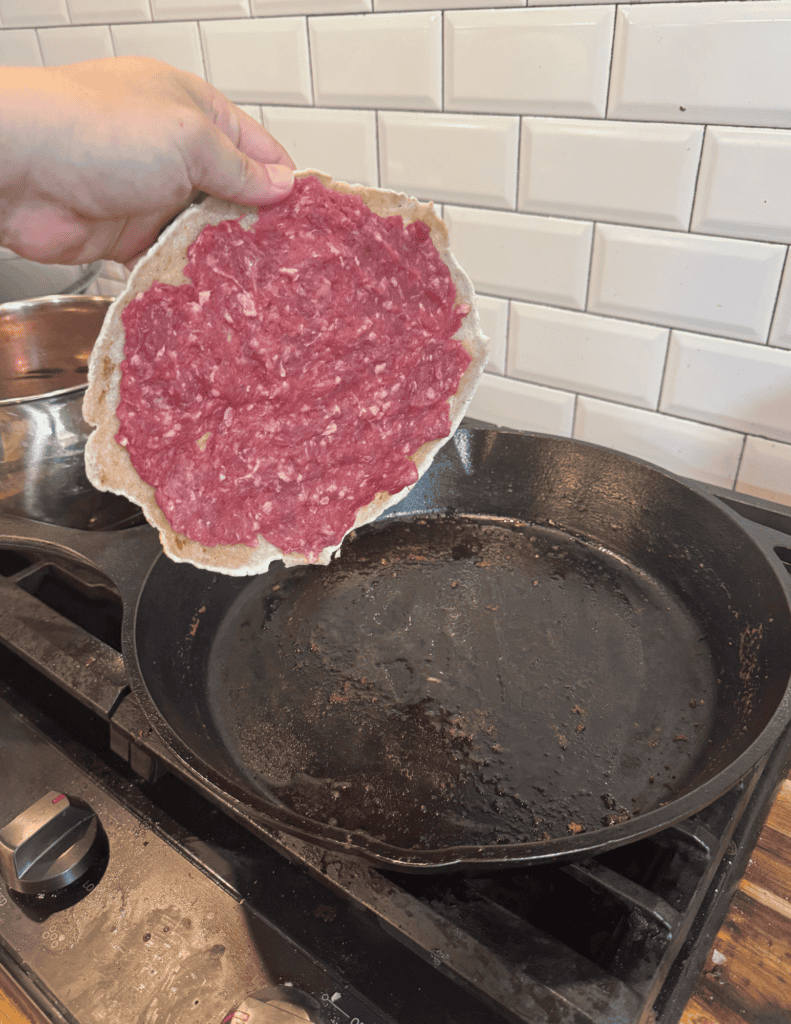 Fresh ground beef pizza being prepared in a skillet.