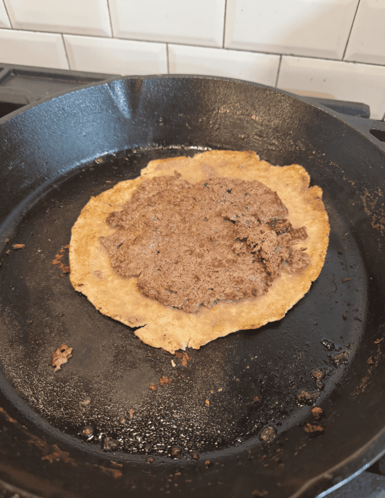 Freshly cooked beef taco in a black skillet with crispy edges and seasoned meat.