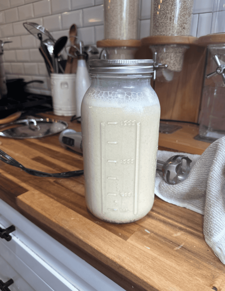 Fresh homemade nut milk in a glass mason jar on a kitchen counter.