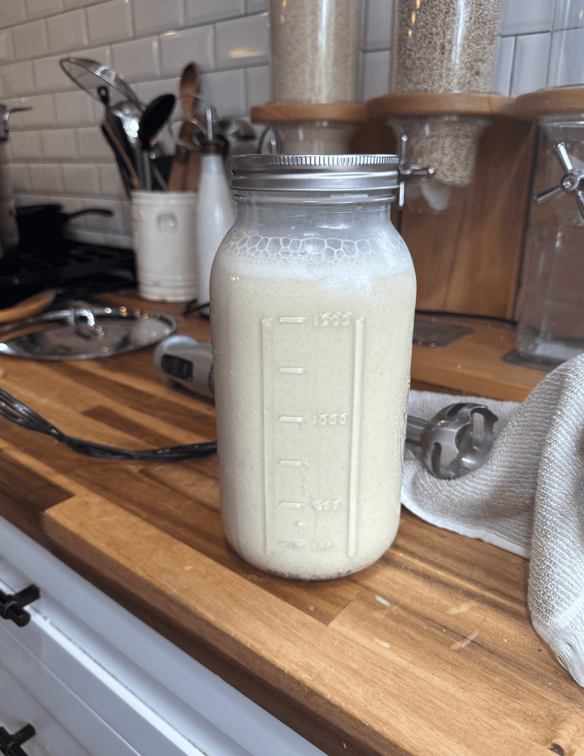 Fresh homemade nut milk in a glass mason jar on a kitchen counter.