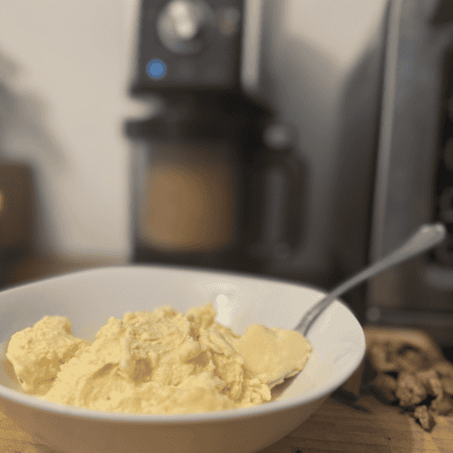 Close-up of scrambled eggs in a white bowl with a spoon on a wooden table.