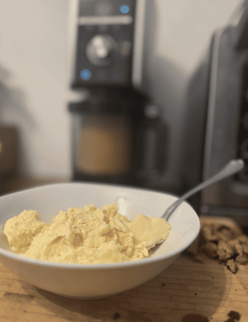 Close-up of scrambled eggs in a white bowl with a spoon on a wooden table.