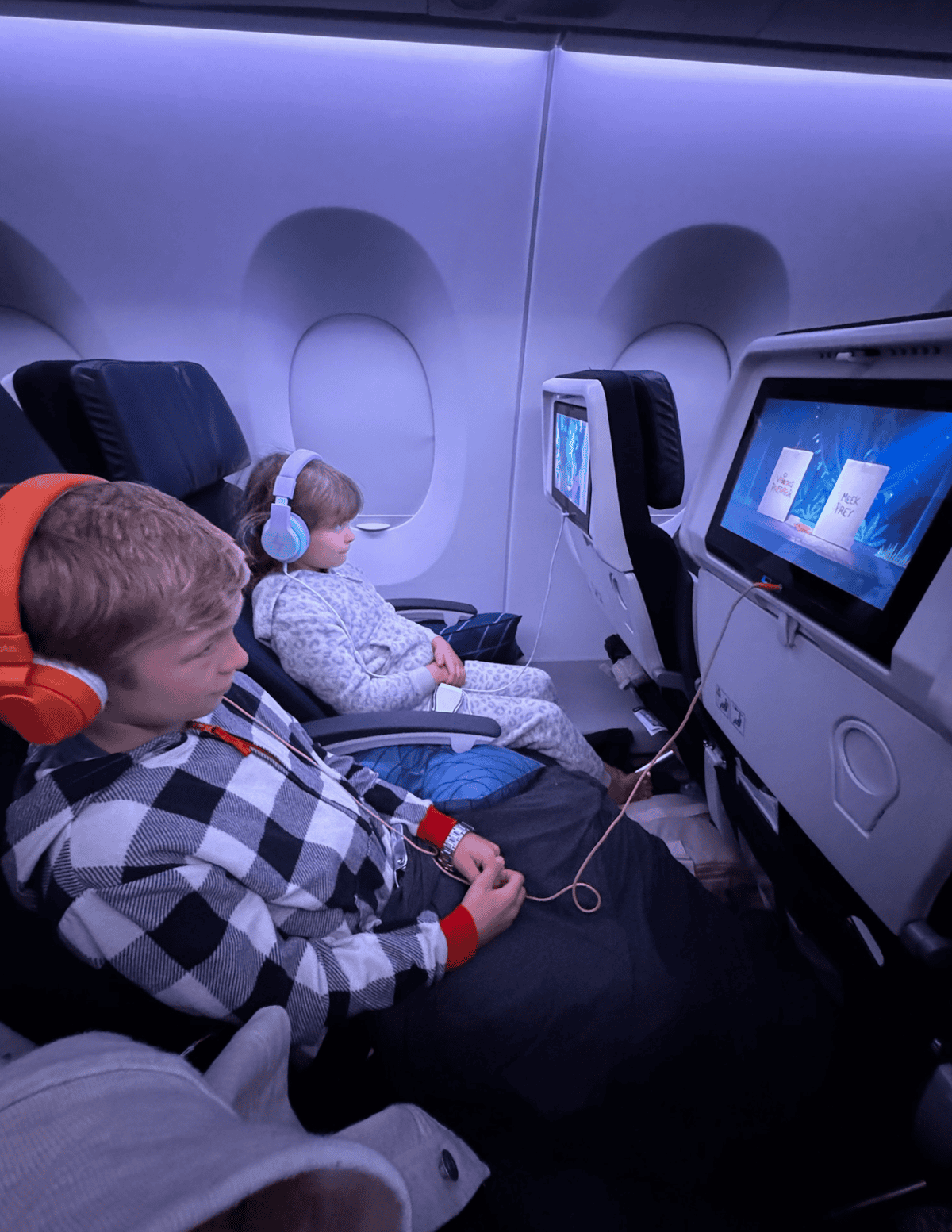 Children enjoying movies on airplane seatback screens during flight.