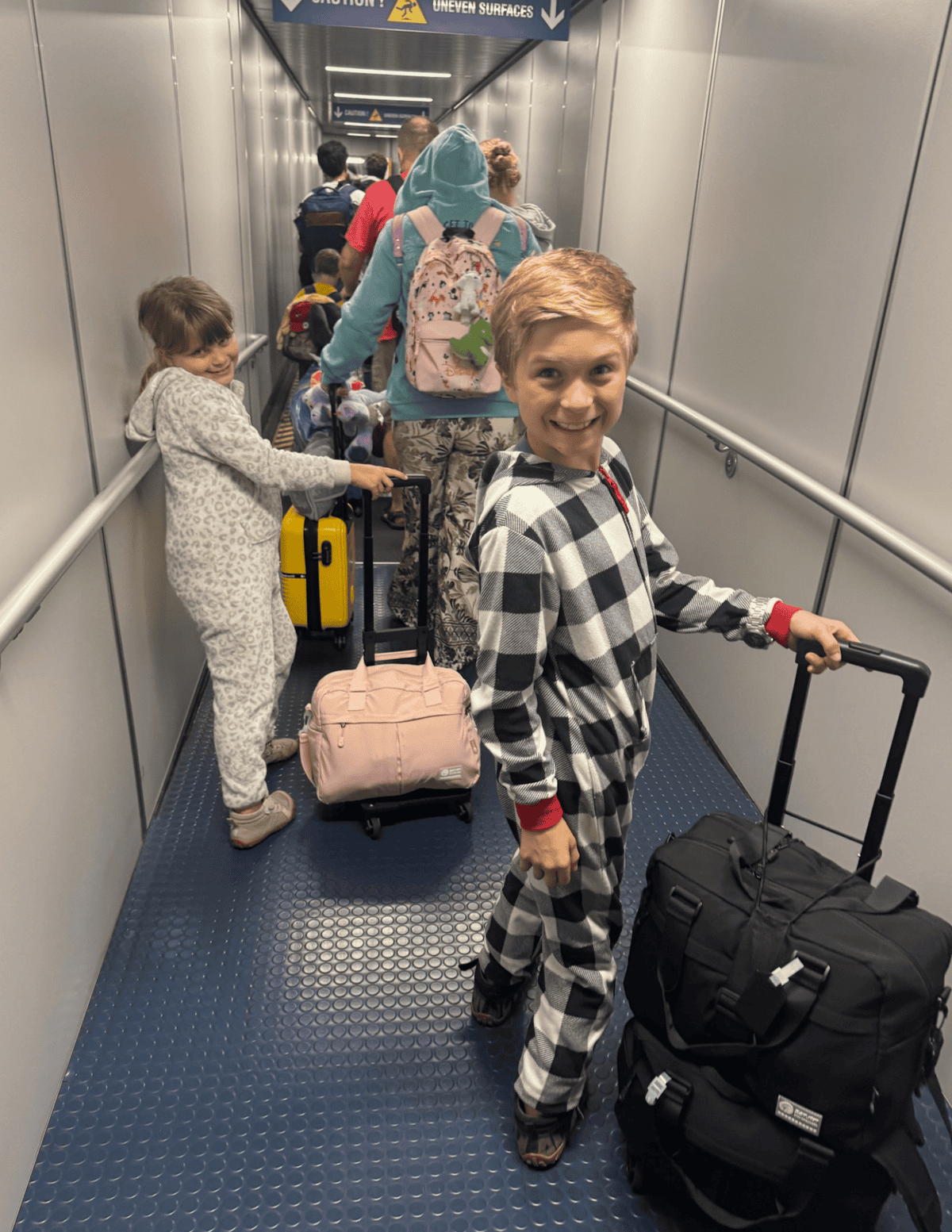 Family with children and luggage waiting at airport gate for flight.