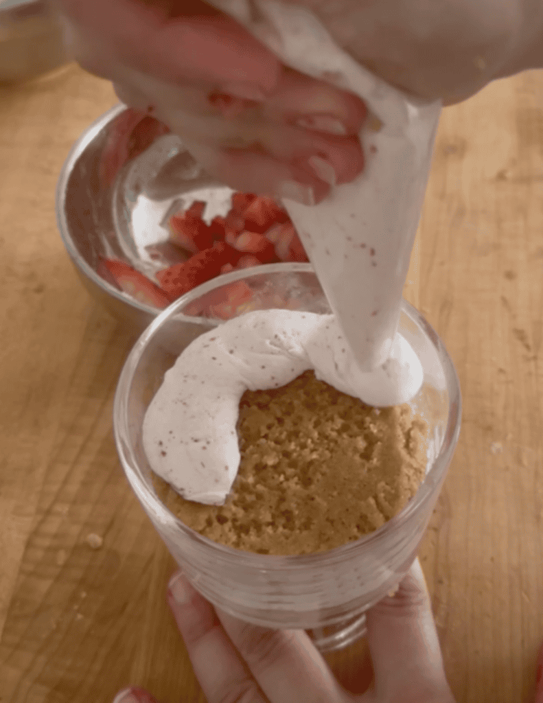 Pouring whipped cream over gluten-free strawberry trifle in a glass.